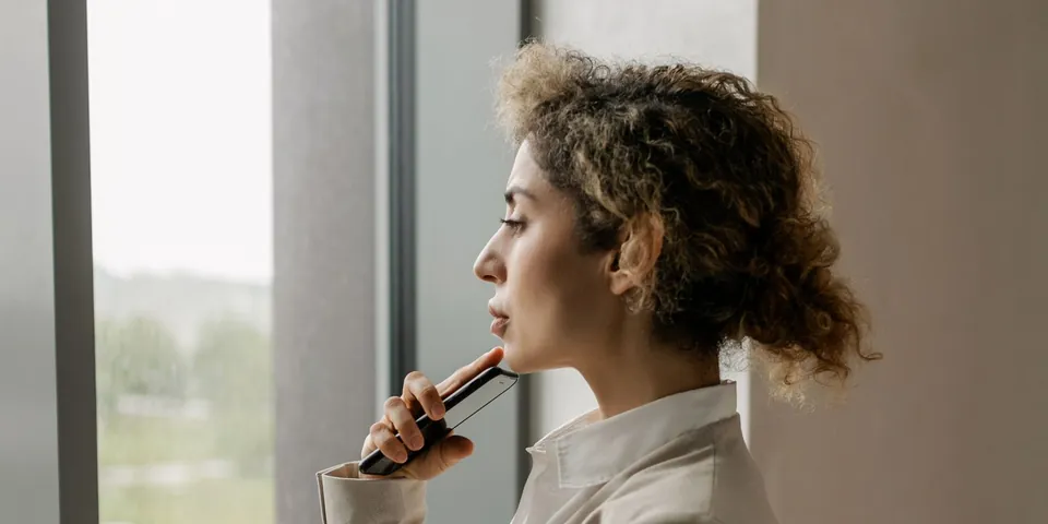 A person in an office pausing by a window, looking out thoughtfully.