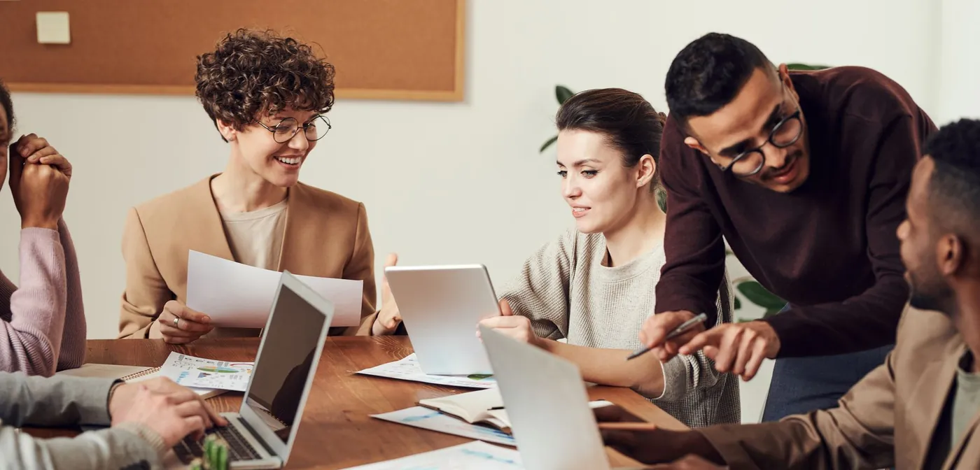 Managers gathered around a table reviewing a tablet and notes together during a working conversation.